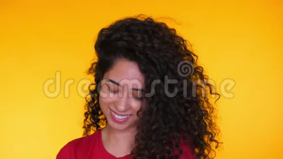 年轻的拉丁女孩在黄色背景上卷发的肖像诱惑女人微笑着对着镜头演播室录像视频的预览图