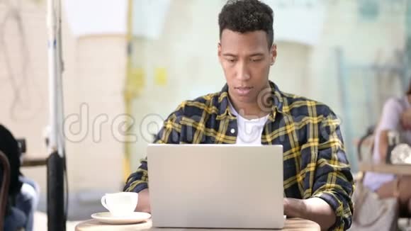 非洲青年男子对笔记本电脑户外咖啡厅的成绩感到沮丧视频的预览图