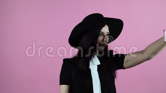 这位女士在粉红色的背景上自拍一个穿着黑色连衣裙和帽子的女人给自己拍照视频的预览图
