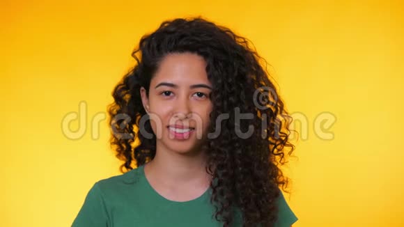 西班牙年轻学生女孩的肖像黄色背景上有卷发时髦可爱的女人对着镜头微笑工作室视频的预览图