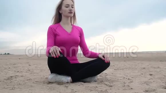 女孩坐在海滩上以莲花的姿势头做体操视频的预览图
