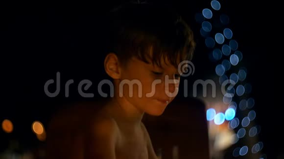 快乐放松的小欧洲男孩吃甜点与大勺子在大气傍晚海滩酒吧与博克灯视频的预览图