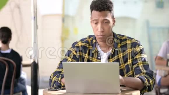 年轻的非洲男人想在笔记本电脑户外咖啡厅中享受震撼视频的预览图