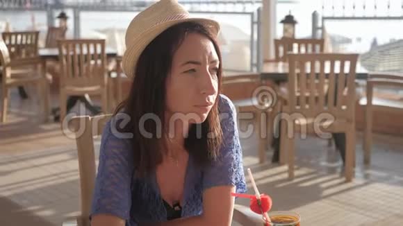 女孩拿着水果鸡尾酒坐在海滩附近的热带咖啡馆里沙滩暑假的概念视频的预览图