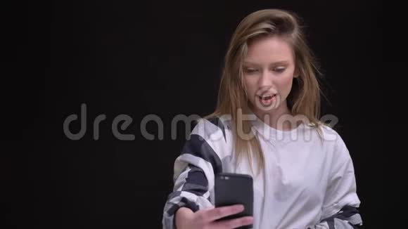 金发白种人长发女孩穿着白色t恤很高兴在黑色智能手机上用视频聊天的画像视频的预览图