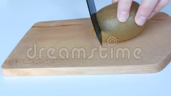 女人的手在厨房的木板上用白色桌子上的黑色陶瓷刀切熟的猕猴桃视频的预览图
