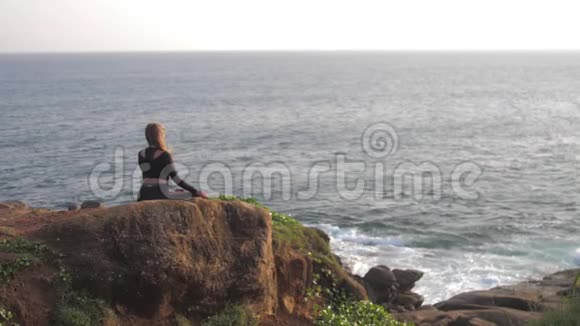 穿着运动服的布鲁内特坐在灰色的岩石悬崖上冥想视频的预览图