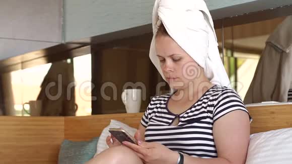 一个头上戴着白色毛巾的女人拿着电话坐在床上视频的预览图