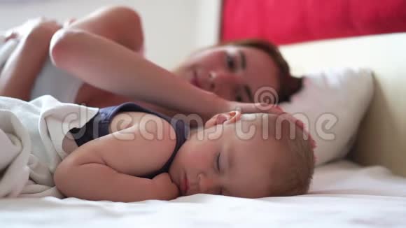 漂亮的年轻妈妈亲吻婴儿的脸颊而他甜蜜地睡觉视频的预览图