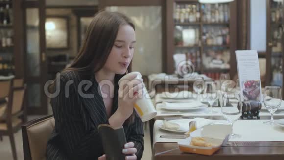 肖像可爱的女人穿着西装坐在餐厅吃快餐可爱的黑发女人喝可乐视频的预览图