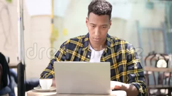 年轻非洲男子颈部疼痛使用笔记本电脑户外咖啡厅视频的预览图