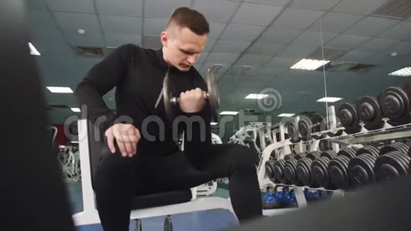 一个体格健壮的人坐着用哑铃交替地训练肌肉的手视频的预览图