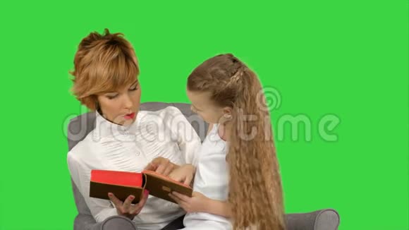 母亲和女儿在绿色屏幕上的沙发上看书Chroma键视频的预览图