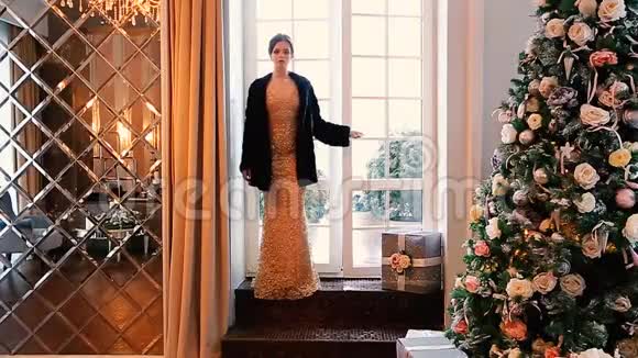 一个穿着晚礼服和黑色貂皮大衣的漂亮女孩走进了装饰着圣诞树的房间视频的预览图