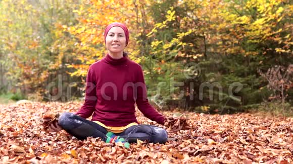 小女孩坐在森林里的一片空地上兴高采烈地抛出黄色的叶子视频的预览图