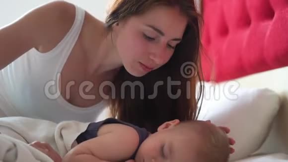 年轻的女人亲吻婴儿的脸颊而他甜蜜地睡在缓慢的动作视频的预览图