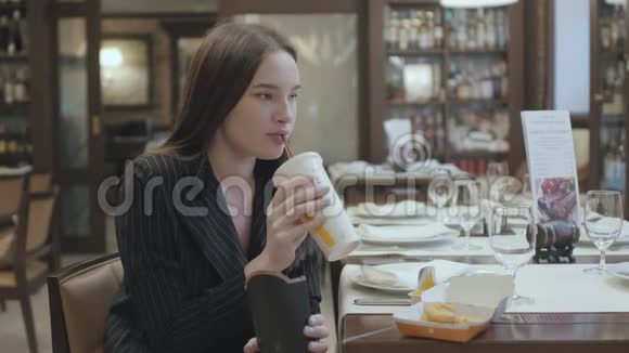 穿西装的漂亮女人坐在餐厅吃快餐漂亮的黑发女人喝可乐吃东西视频的预览图