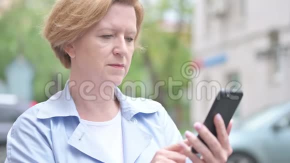 户外老女人在使用智能手机时为成功而兴奋视频的预览图