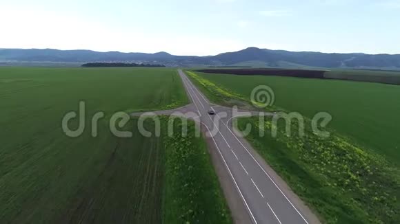 空中勘测黑色的汽车在绿色的田野间沿着公路行驶视频的预览图