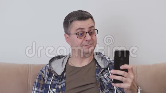 一个中年男人坐在沙发上用智能手机拍照做鬼脸做傻瓜视频的预览图