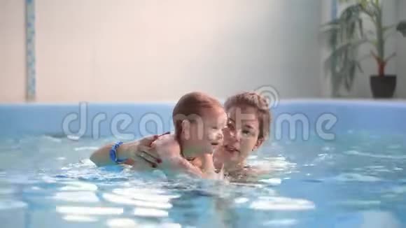 可爱的小宝宝和他妈妈在游泳池里上游泳课妈妈把儿子抱在手里视频的预览图