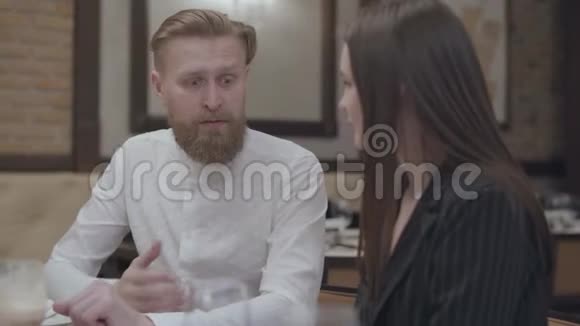 美丽的黑发女人和一个英俊的胡须金发男人坐在桌子旁那个男人给他女朋友讲故事视频的预览图
