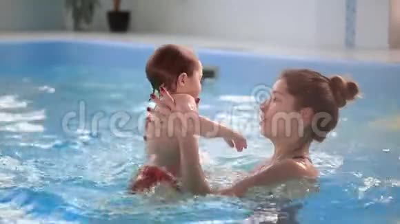 可爱的小宝宝和他妈妈在游泳池里上游泳课妈妈把儿子抱在手里视频的预览图