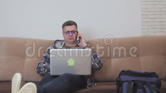 一个坐在沙发上的中年男子正在用笔记本电脑和电话交谈旁边是一个大型旅游背包视频的预览图