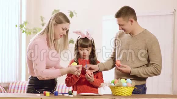 一家人带着女儿家里装饰的复活节彩蛋摆在桌子上是颜料和一篮子彩蛋视频的预览图