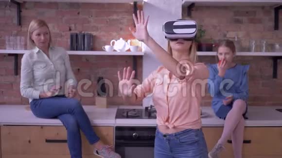 技术VR年轻女性进入虚拟现实头盔与家庭在厨房玩现代游戏视频的预览图