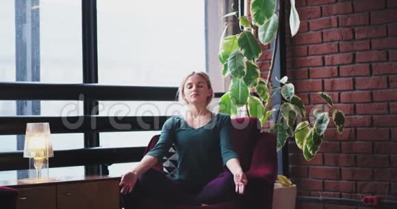 在一个现代化的城市设计场所一位女士早上在红色沙发上练习瑜伽冥想姿势她关门了视频的预览图