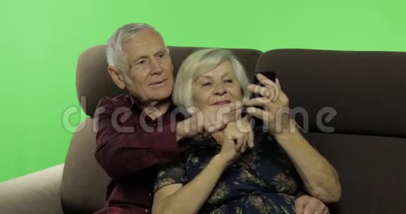 年长的男人和女人坐在沙发上做智能手机视频的预览图