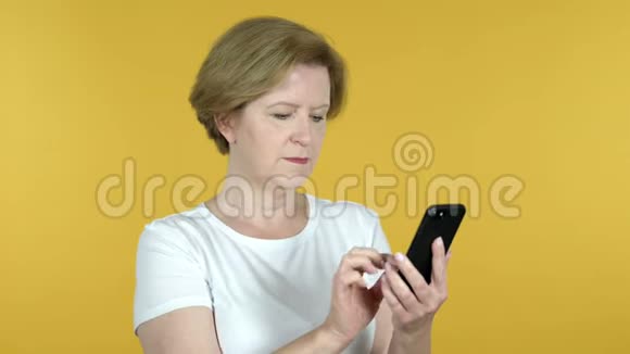 黄色背景下的老女人浏览智能手机视频的预览图