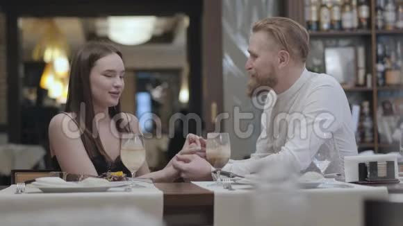肖像可爱的黑发女人和一个英俊的胡须金发男人坐在对方面前的桌子旁那个人视频的预览图
