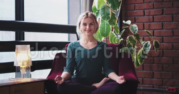 一位心情愉快的女士微笑着在家里的沙发上练习瑜伽冥想姿势在现代客厅的氛围中4k视频的预览图