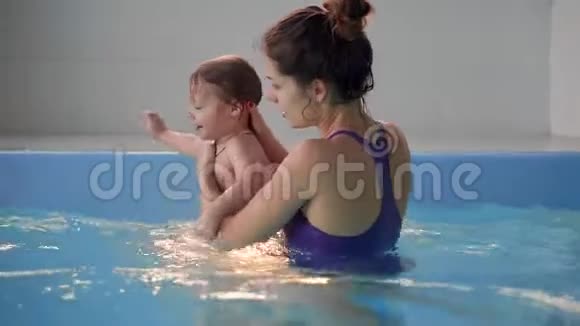 美丽的妈妈教可爱的宝贝女孩如何在游泳池里游泳孩子和妈妈在水里玩视频的预览图