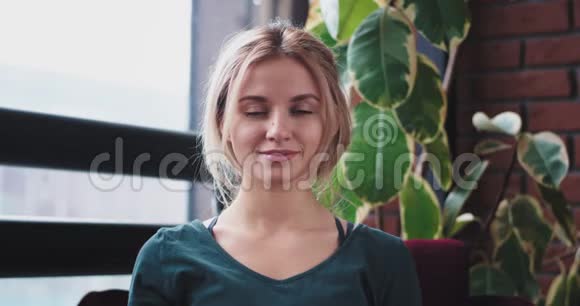 漂亮的金发女士直视着相机微笑着坐在家里的沙发上穿着家庭服装4k视频的预览图