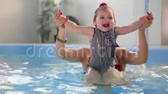 戴着防护眼镜的可爱金发幼儿正和他的母亲一起在游泳池里潜水视频的预览图