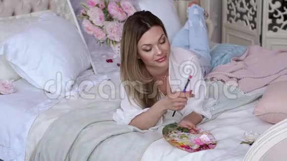 一个女孩艺术家的肖像在床上的房子手里拿着调色板视频的预览图