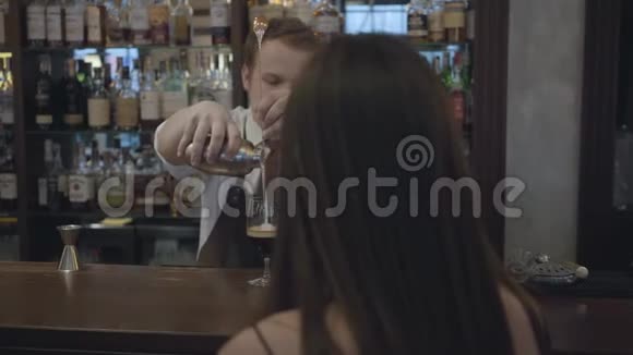 在酒吧柜台坐着一个面目全非的黑发女人在杯子里倒两份浓缩咖啡的酒保视频的预览图