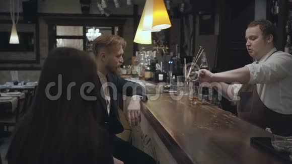 坐在酒吧柜台前的那个留着胡子的年轻男人和面目全非的黑发女人一个倒酒的酒保视频的预览图