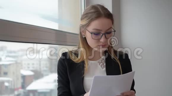 女金融家看着商务文件站在办公室的窗口视频的预览图