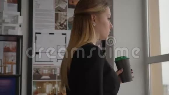 年轻的女设计师手拿着咖啡杯在窗前喝着视频的预览图