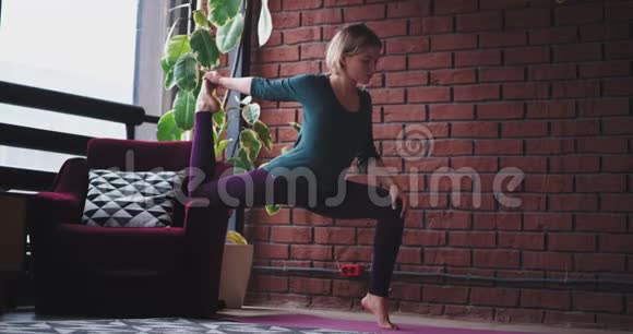 漂亮的年轻女士穿着运动服在家里用沙发做一个艰苦的运动用瑜伽通奸来伸展身体视频的预览图