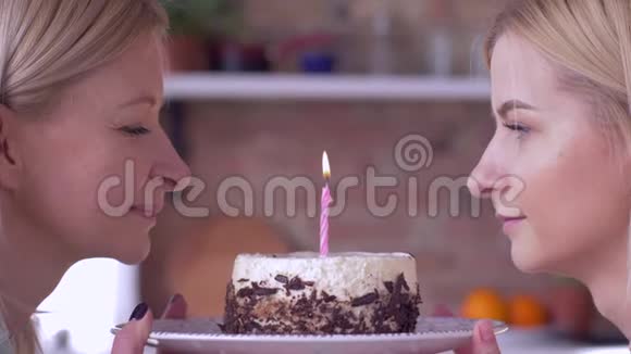 祝你生日快乐妈妈和成年女儿一起在节日蛋糕上吹蜡烛微笑着互相看着视频的预览图