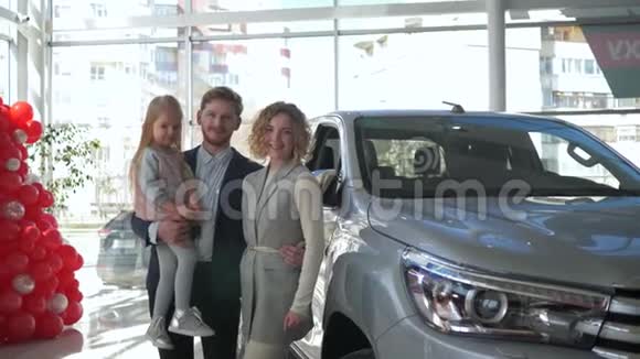 一对带着小女儿的微笑家庭夫妇的画像展示了在汽车沙龙购买的汽车钥匙视频的预览图