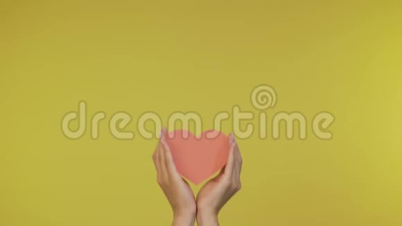 女性的手轻轻地拿着一张纸大大的心在一个孤立的黄色背景上4k视频的预览图