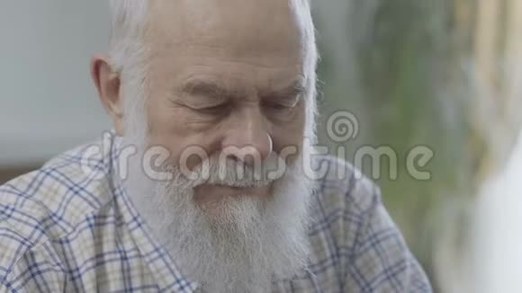 坐在家中坐得近的有着深思熟虑的胡须的成熟男人的肖像老人感到不舒服老人有一个视频的预览图