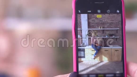 手机上的照片年轻风趣的女人在厨房里的智能手机上摆姿势拍照视频的预览图