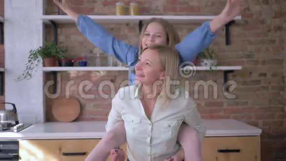 和妈妈一起玩游戏有趣的小女孩和妈妈坐在后面在家庭厨房里做手臂伸展的飞机视频的预览图